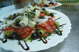 Griechischer Bauernsalat mit grünem Salat, Oliven, Zwiebelringen, Tomatenscheiben, Weißkäse, Basilikum und Balsamico